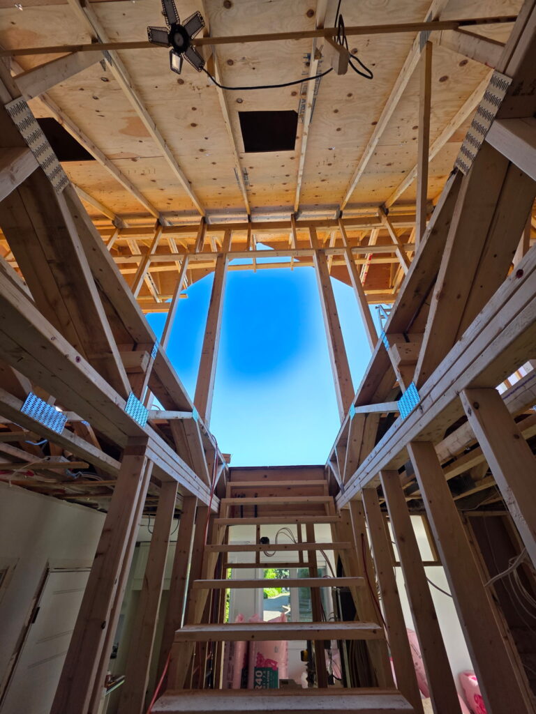 Structure en bois d’un agrandissement résidentiel en cours de construction en Estrie, montrant la charpente d’un ajout d’étage avec ossature apparente et ouverture centrale.